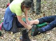 Person applying a bandage to another person's foot in a forest setting