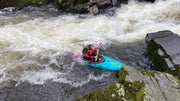 Person kayaking in a river with rapids and rocks